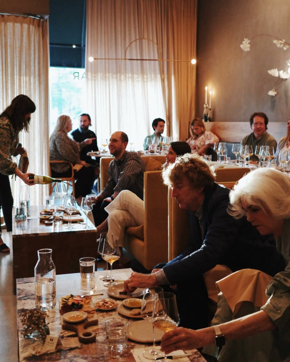 8 Ways to Meet New People in BHAM - 7 People enjoy drinks and small plates at Golden Age Wine. A server pours wine at one table. The atmosphere is warm with soft lighting and casual conversation.