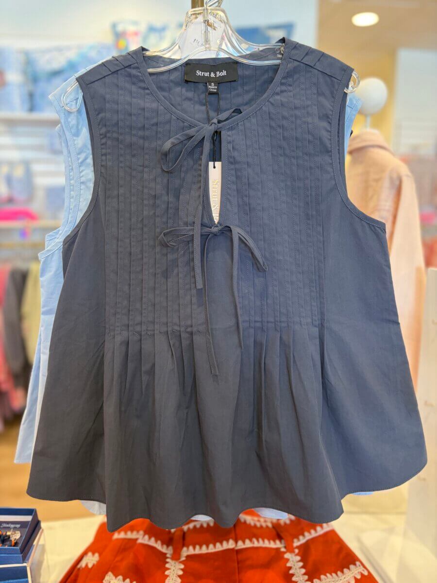 Sleeveless navy blue blouse with front ties and pleated detailing, perfect for those Weekend Finds, displayed on a hanger in a clothing store.