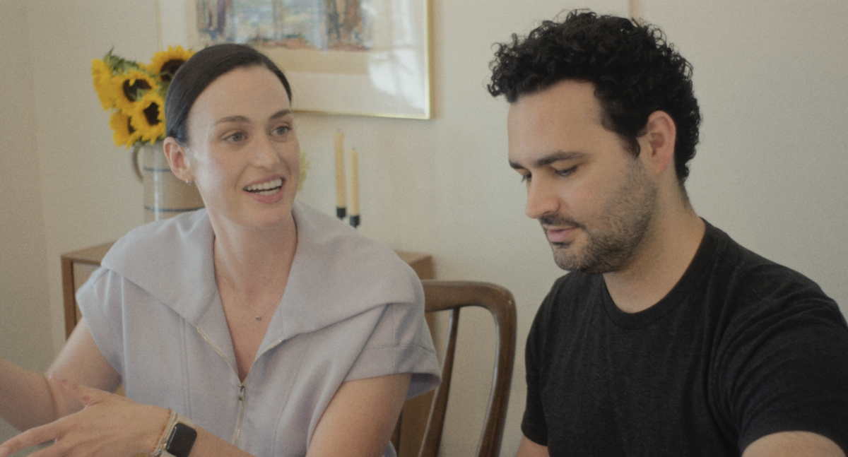 How Food & Family Carried One Alabama Woman Through IVF (+ 3 Recipes) - 2 A woman gestures and smiles while talking to a man who is looking down, perhaps sharing insights from her fertility journey. They are seated at a table in a room with sunflowers and framed art in the background.