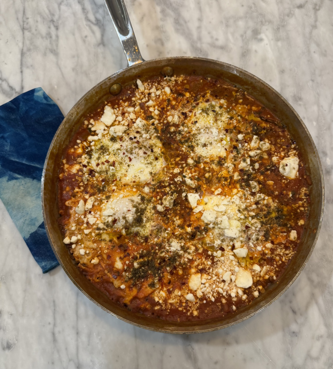 How Food & Family Carried One Alabama Woman Through IVF (+ 3 Recipes) - 6 A skillet of shakshuka with poached eggs, tomato sauce, crumbled feta, and herbs sits on a marble countertop next to a blue patterned napkin.