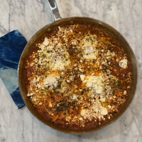 How Food & Family Carried One Alabama Woman Through IVF (+ 3 Recipes) - 7 A skillet of shakshuka with poached eggs, tomato sauce, crumbled feta, and herbs—perfect as one of your fertility recipes—sits on a marble countertop next to a blue patterned napkin.