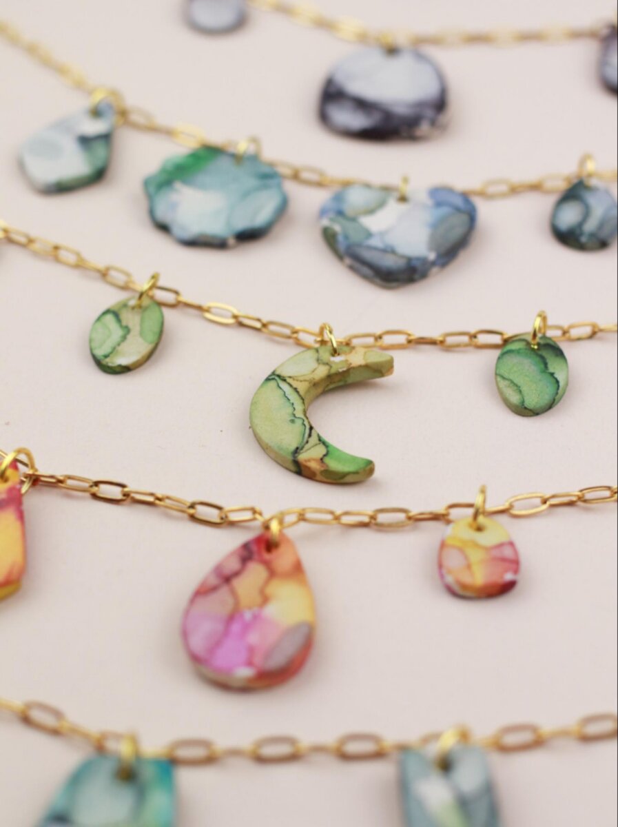 She Brings Art, Vintage Finds & Creativity to Memphis - 3 Close-up of gold chain necklaces with pendants in various shapes and colors, including crescent moon, teardrop, and heart, displayed on a neutral background.