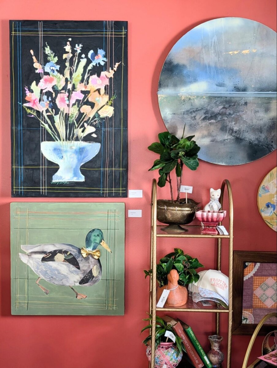 She Brings Art, Vintage Finds & Creativity to Memphis - 6 A wall with pink paint displays two paintings, a round mirror, a shelf holding a plant, decorative items, and several small objects.