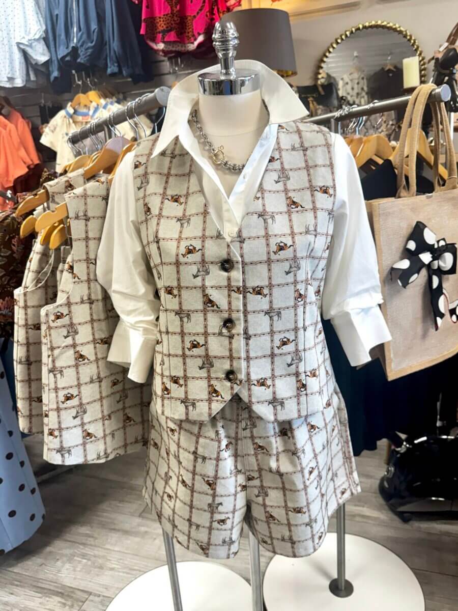 A mannequin wears a white shirt with rolled sleeves, a matching plaid vest, and shorts, displayed in a clothing store with other garments and accessories visible in the background as part of the Fall Preview collection from Louisville FINDS.