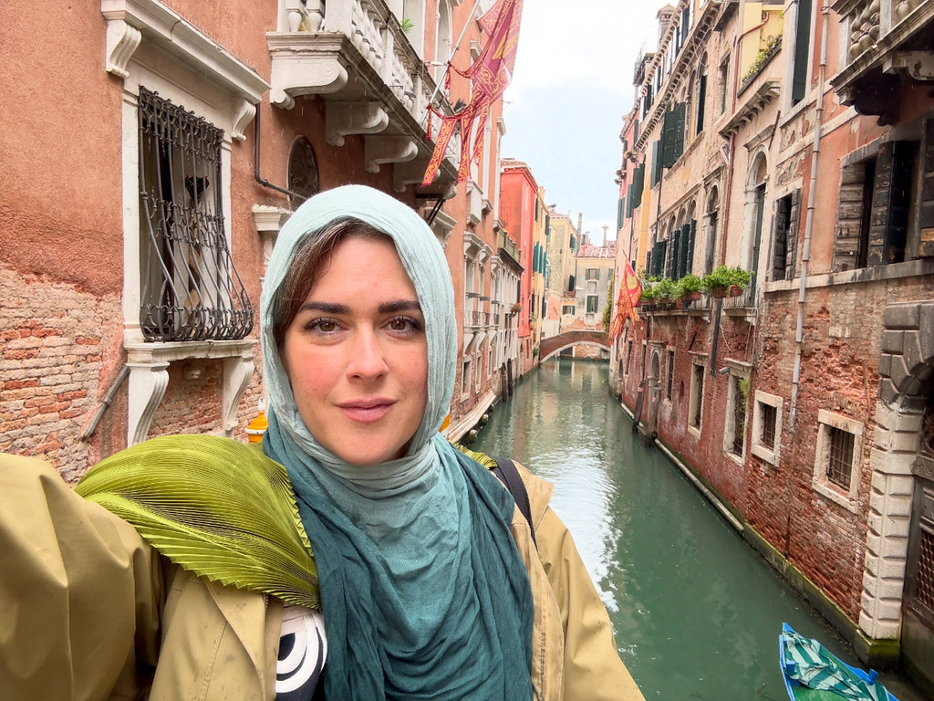 Meet the Woman Behind Louisville's First Children's Museum - 6 A woman in a light blue hijab takes a selfie in front of a narrow Venetian canal with colorful buildings and arched bridges.
