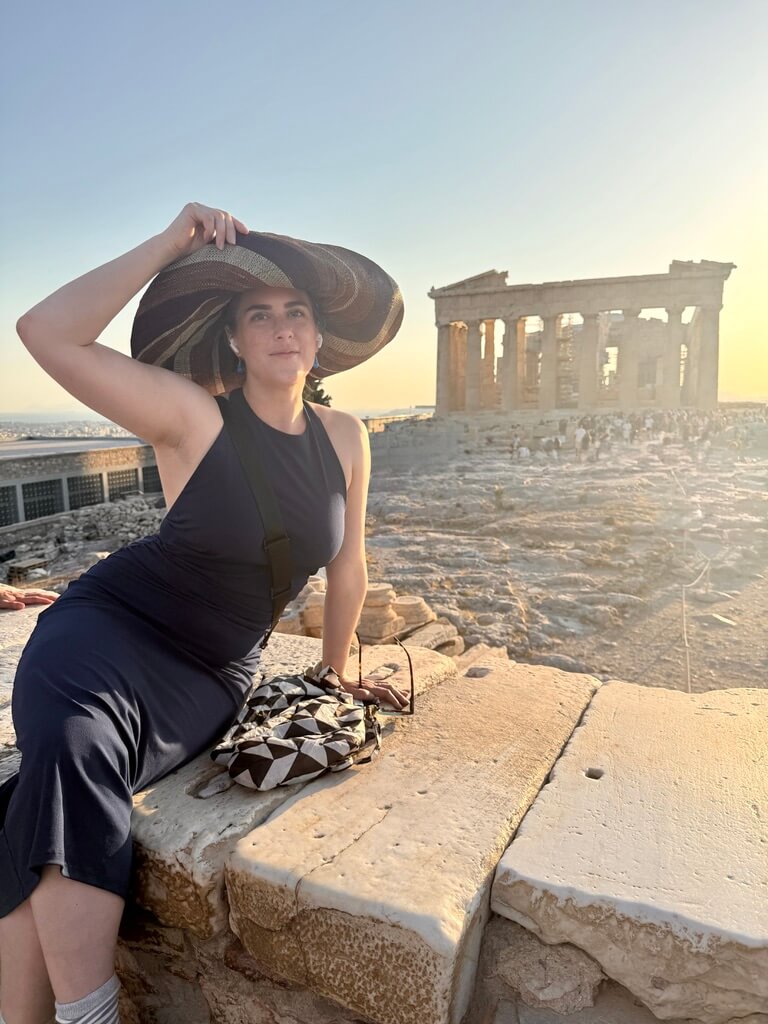 Meet the Woman Behind Louisville's First Children's Museum - 7 A person in a large sunhat and dark dress sits on a stone ledge at the Acropolis in Athens, with the Erechtheion temple in the background at sunset.