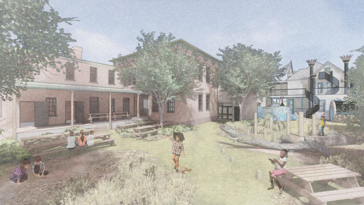 Meet the Woman Behind Louisville's First Children's Museum - 3 Children engage in Child’s Play as they play and sit on benches in a landscaped outdoor area with trees, grass, and play structures, surrounded by brick and white buildings.