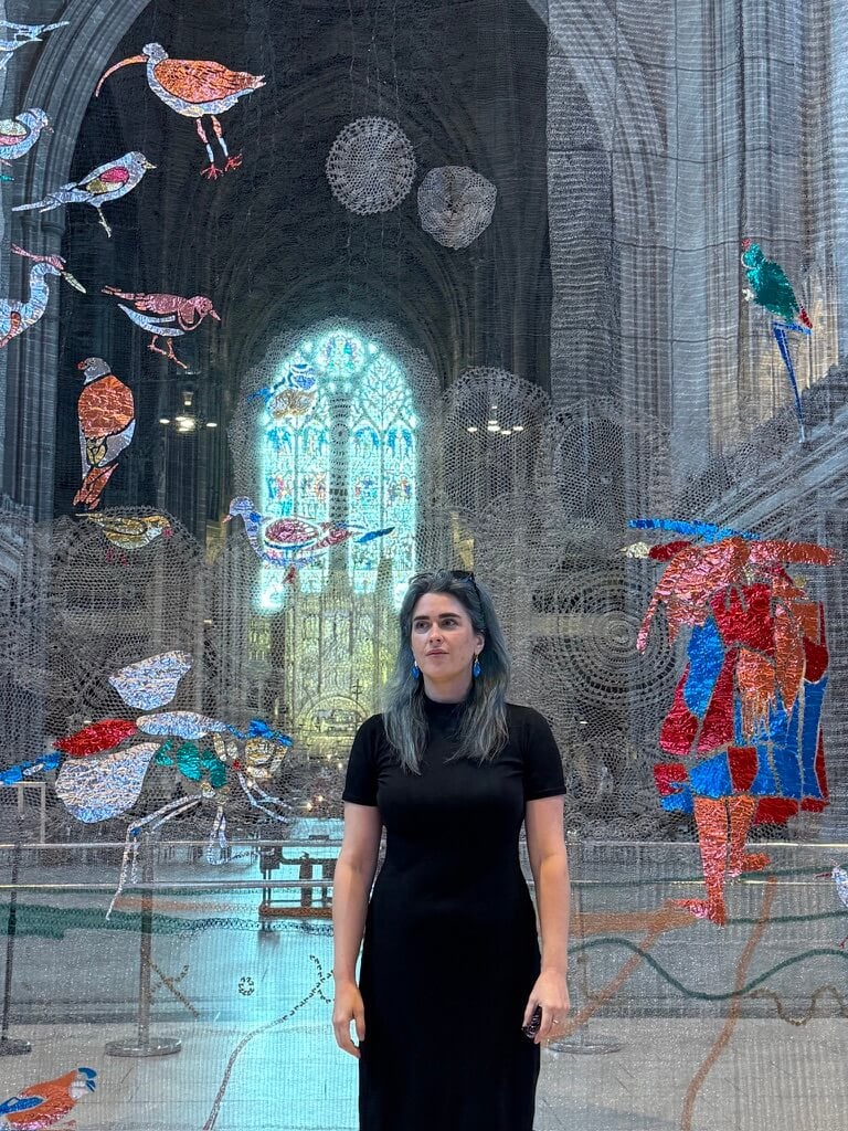 Meet the Woman Behind Louisville's First Children's Museum - 2 A woman in a black dress stands in front of a colorful, bird-themed art installation inside a large, ornate cathedral with stained glass windows.