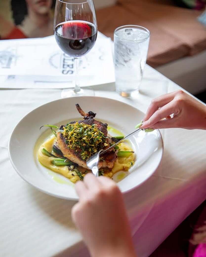 The Best of Lexington, KY: Iconic Stops + Hidden Gems - 2 A person cuts into a plated dish topped with greens, next to a glass of red wine and a glass of water on a white tablecloth.
