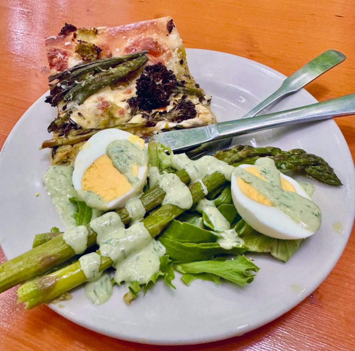 The Best of Lexington, KY: Iconic Stops + Hidden Gems - 7 A white plate with two pizza slices, hard-boiled egg halves, asparagus, mixed greens, and green dressing sits on a wooden table with a fork and knife.