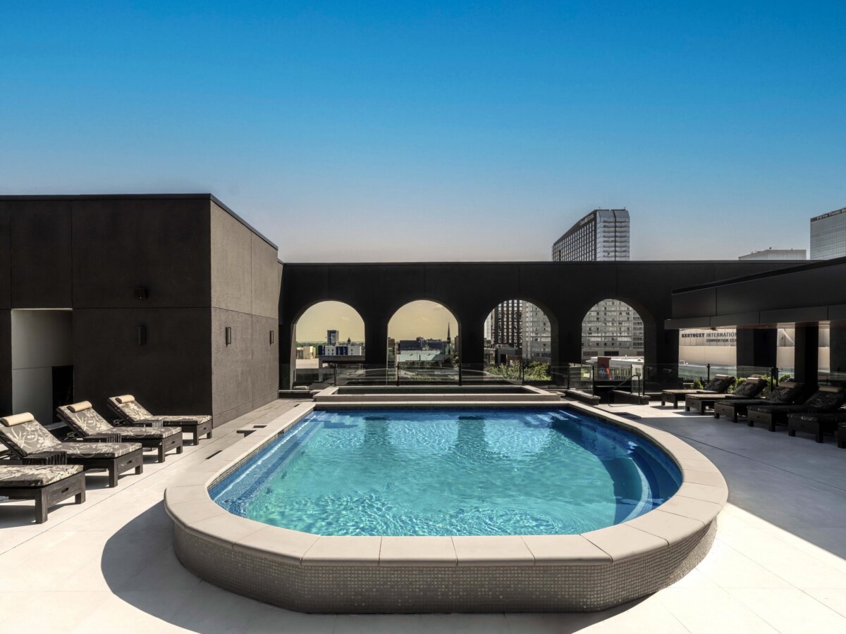 Your Guide to Boutique Hotels in Louisville - 4 Rooftop pool surrounded by lounge chairs, with arched openings showing a city skyline under a clear blue sky—an inviting retreat found in some of the finest Louisville hotels.