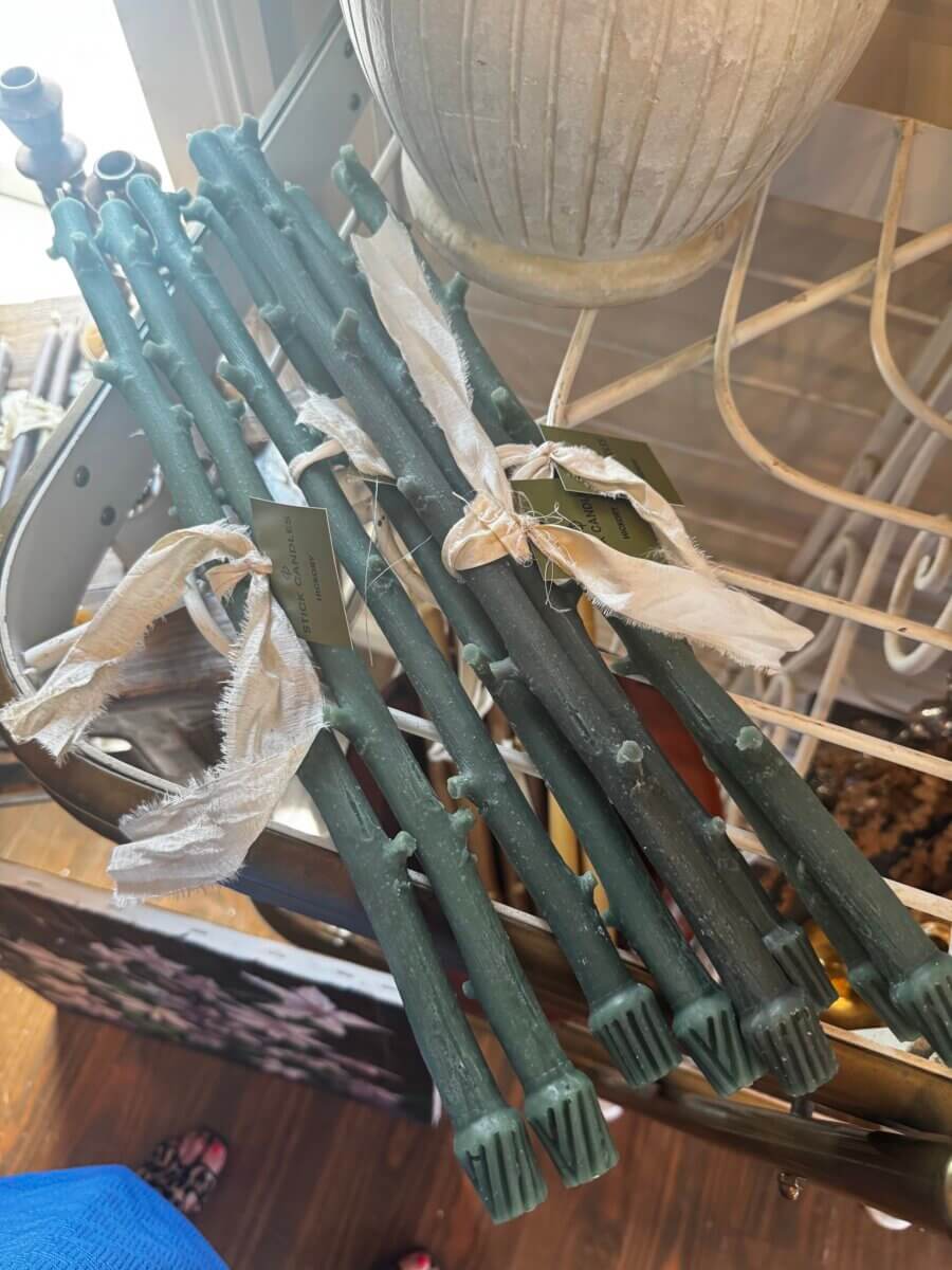 A bundle of green candles with imitation branch texture and cloth tags, displayed on a wooden surface near a white pot.