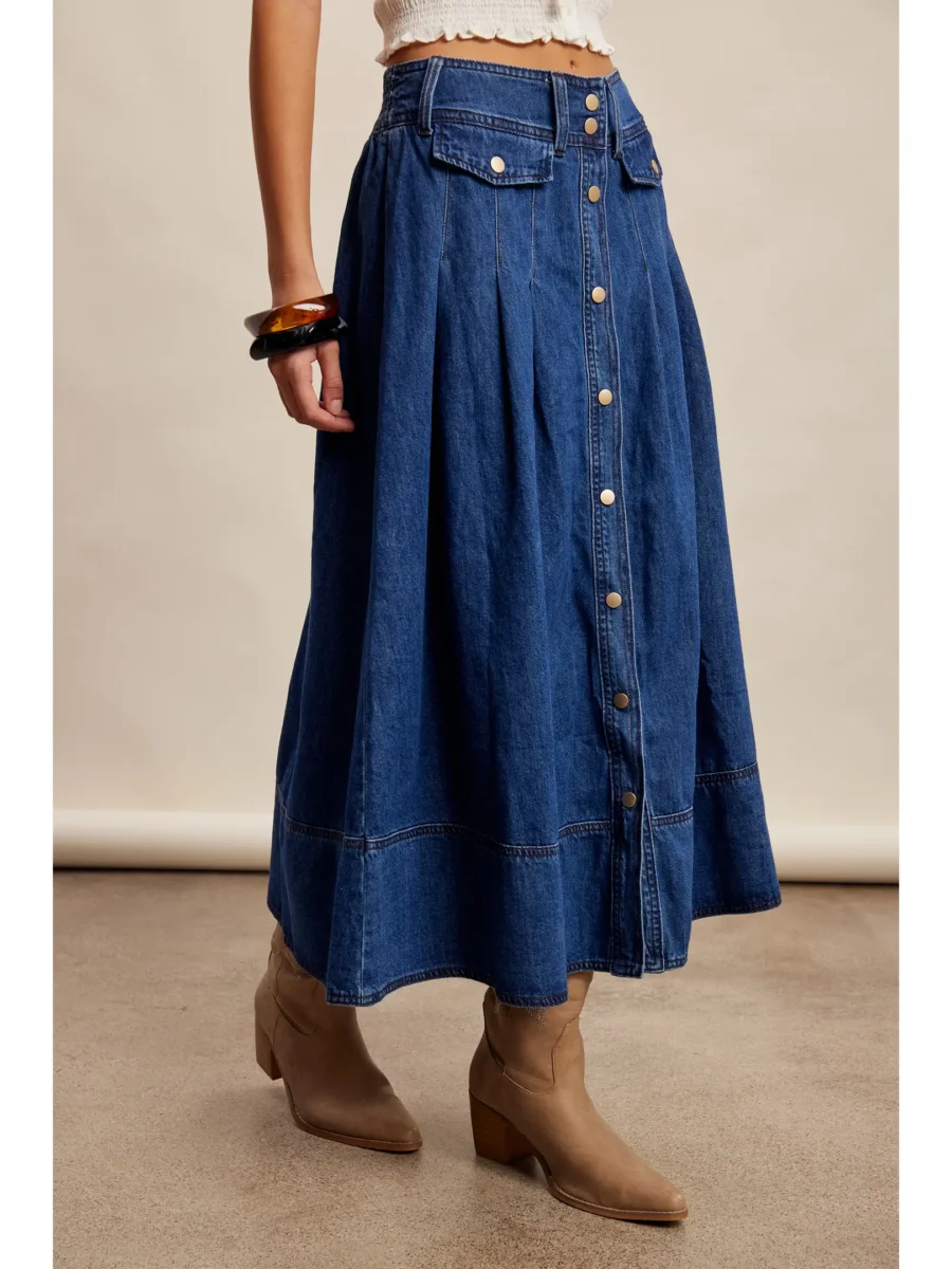 A person wearing a high-waisted, button-front blue denim midi skirt, tan ankle boots, and chunky bracelets, standing on a neutral floor.