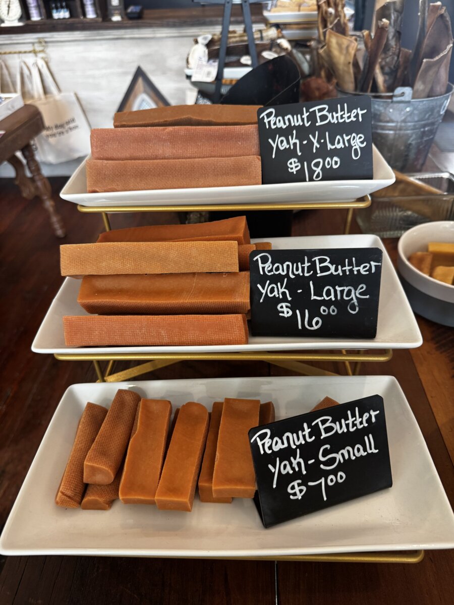 Three trays display peanut butter yak treats in small, large, and extra large sizes, each labeled with prices on chalkboard signs in a shop setting.