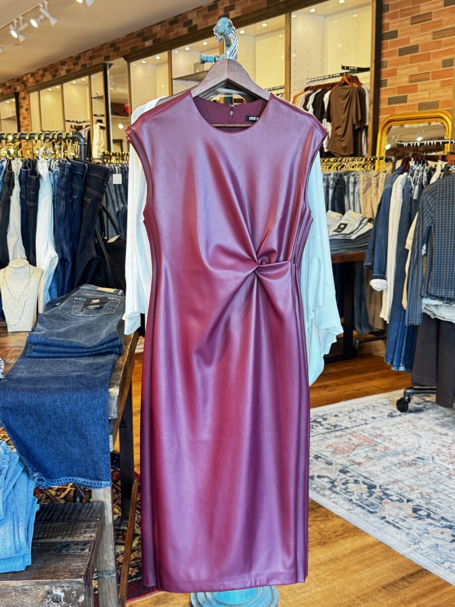 Sleeveless maroon faux leather dress with side knot detail displayed on a hanger in a clothing store.