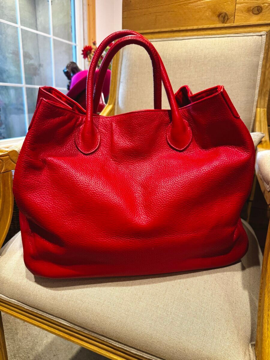 A large red leather handbag, featured in our Louisville FINDS Fall Preview, sits on a beige cushioned chair with wooden armrests in a well-lit room.