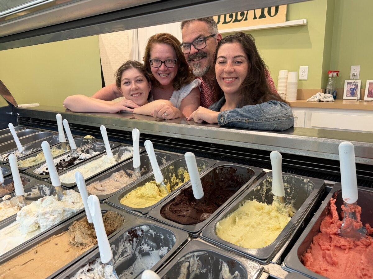 Meet the Art Historian Behind Louisville’s Gelato Gilberto - 5 Four people smile behind a glass counter displaying various flavors of gelato or ice cream in metal tubs with white scoops.