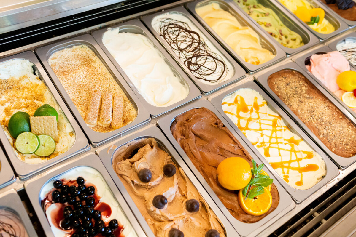 Meet the Art Historian Behind Louisville’s Gelato Gilberto - 3 Assorted gelato flavors displayed in a metal case, including chocolate, fruit, and nut varieties, some topped with fruit slices, sauces, or cookies—each scoop inviting you to experience The Sweet Life.