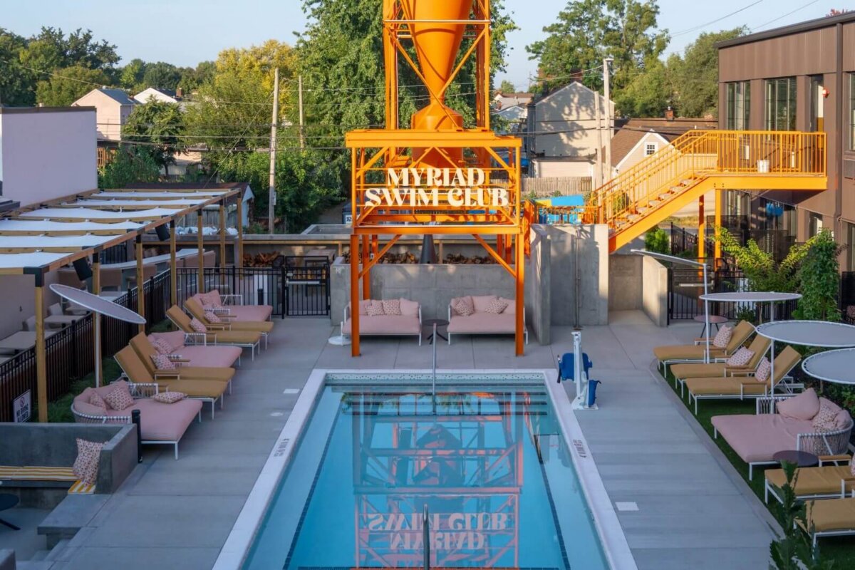 Your Guide to Boutique Hotels in Louisville - 6 A rectangular outdoor pool with lounge chairs on both sides, an orange water tower labeled “MYRIAD SWIM CLUB,” and a staircase in the background evoke the stylish ambiance of boutique hotels found in Louisville.
