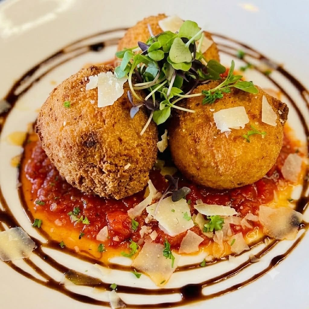 3 New Louisville Restaurants to Try (Plus 3 New Menus!) - 2 Three breaded arancini balls on tomato sauce, garnished with microgreens, shaved cheese, herbs, and a balsamic glaze drizzle on a white plate.