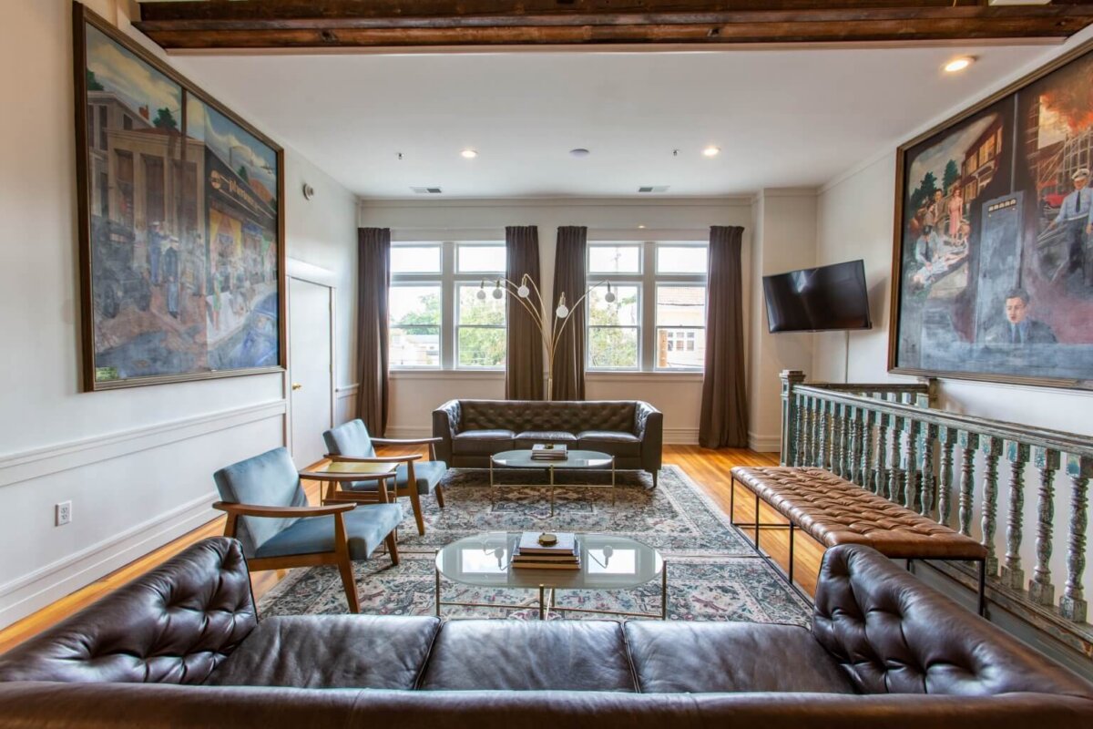Your Guide to Boutique Hotels in Louisville - 3 A modern living room in the style of Louisville’s chic boutique hotels, featuring leather sofas, armchairs, a glass coffee table, large paintings on the walls, and windows letting in natural light.