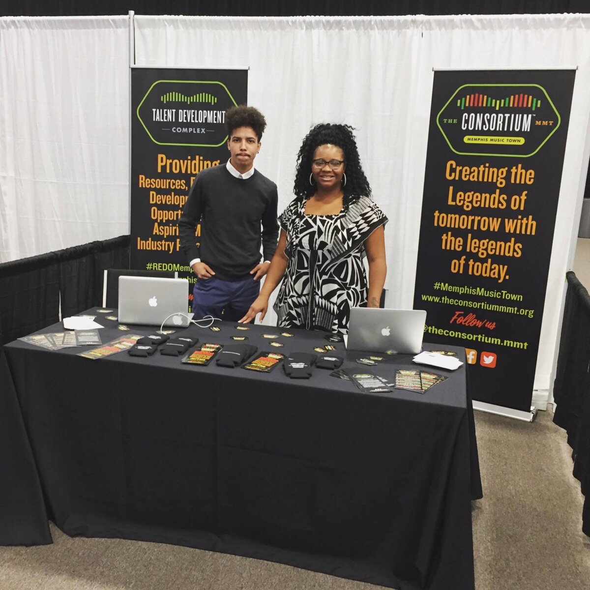Two people stand at a table, giving away swag.