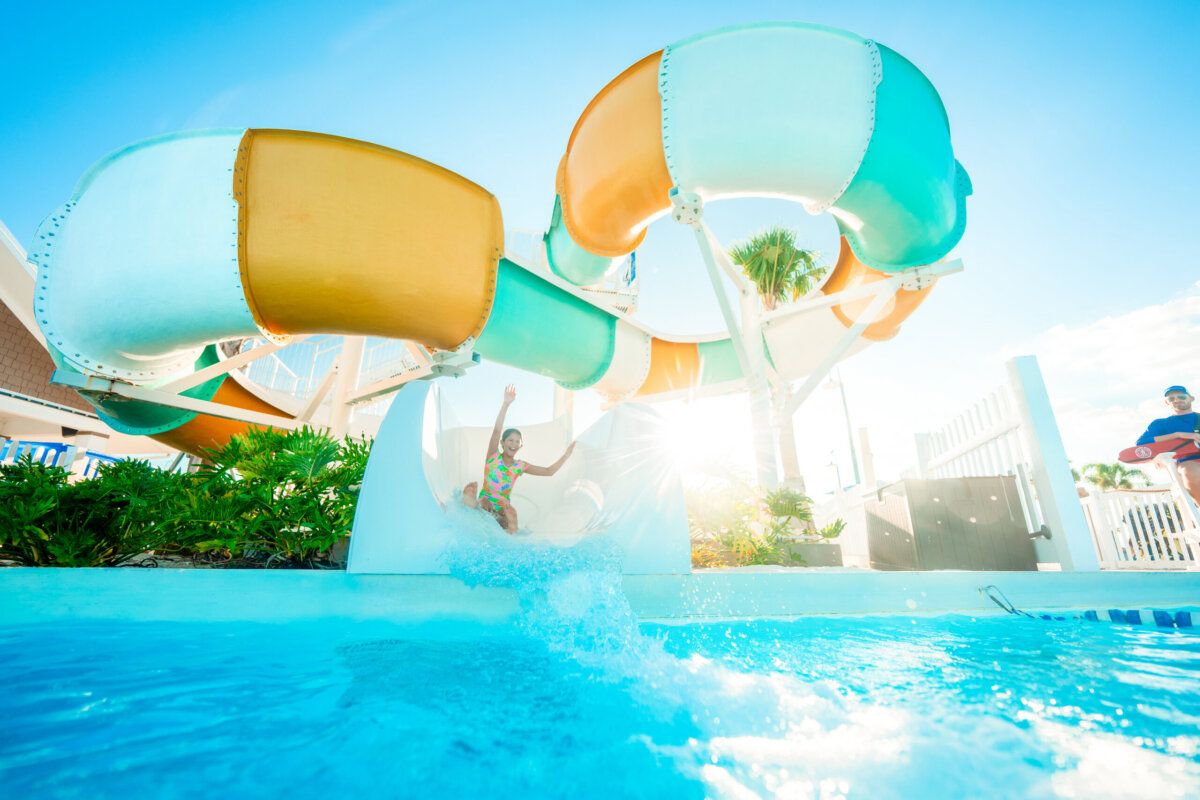 Beyond the Beach: A Weekend Exploring Fort Myers, Sanibel & Captiva - 8 A child slides down a colorful water slide into a pool on a sunny day, with palm trees and a fence in the background, capturing the fun-filled atmosphere typical of Captiva and Sanibel near Fort Myers.
