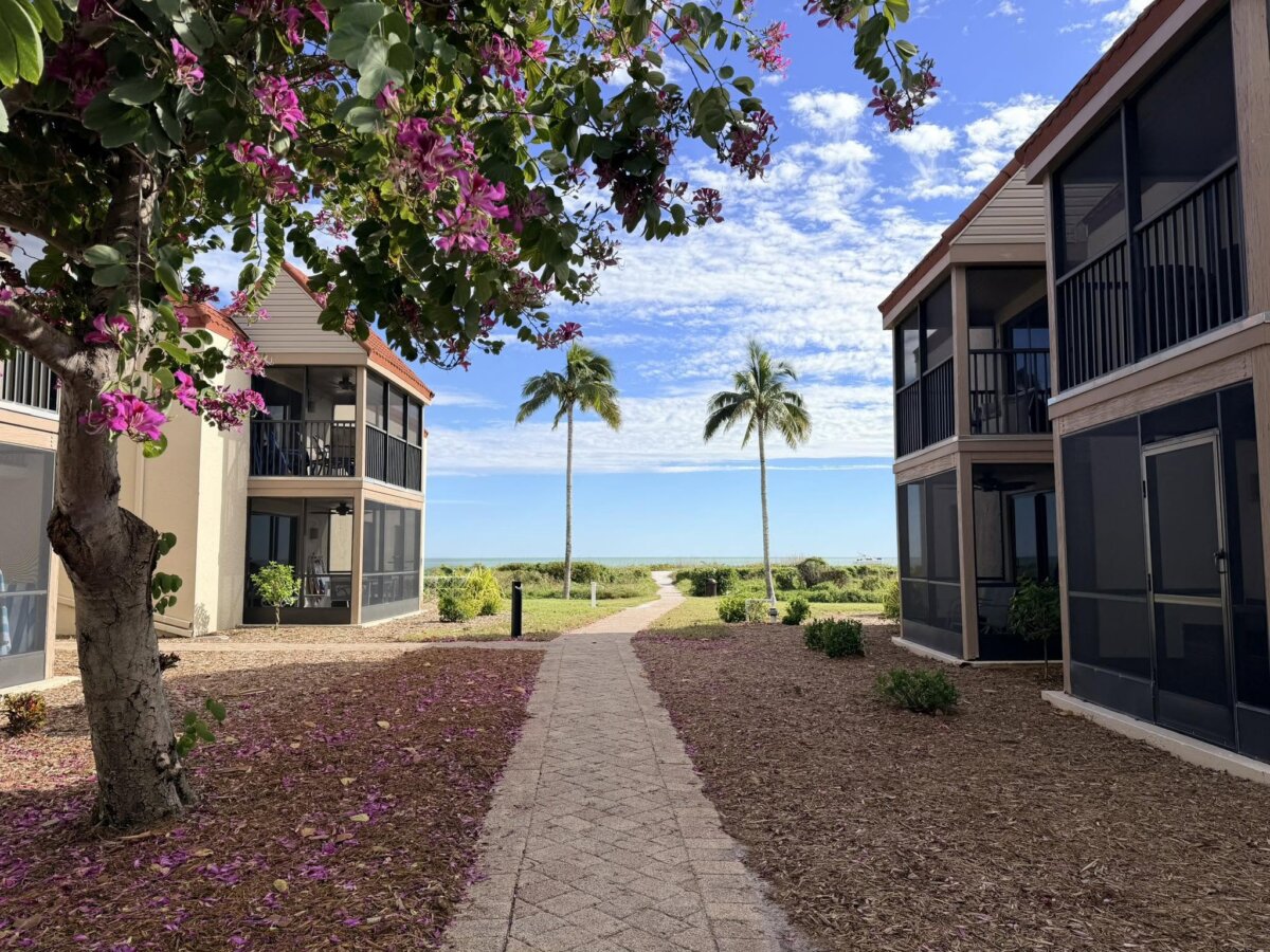 Beyond the Beach: A Weekend Exploring Fort Myers, Sanibel & Captiva - 3 A paved walkway between two buildings with screened balconies, leading to palm trees and a view of the ocean under a partly cloudy sky, evokes the tranquil charm of Captiva and Sanibel near Fort Myers.