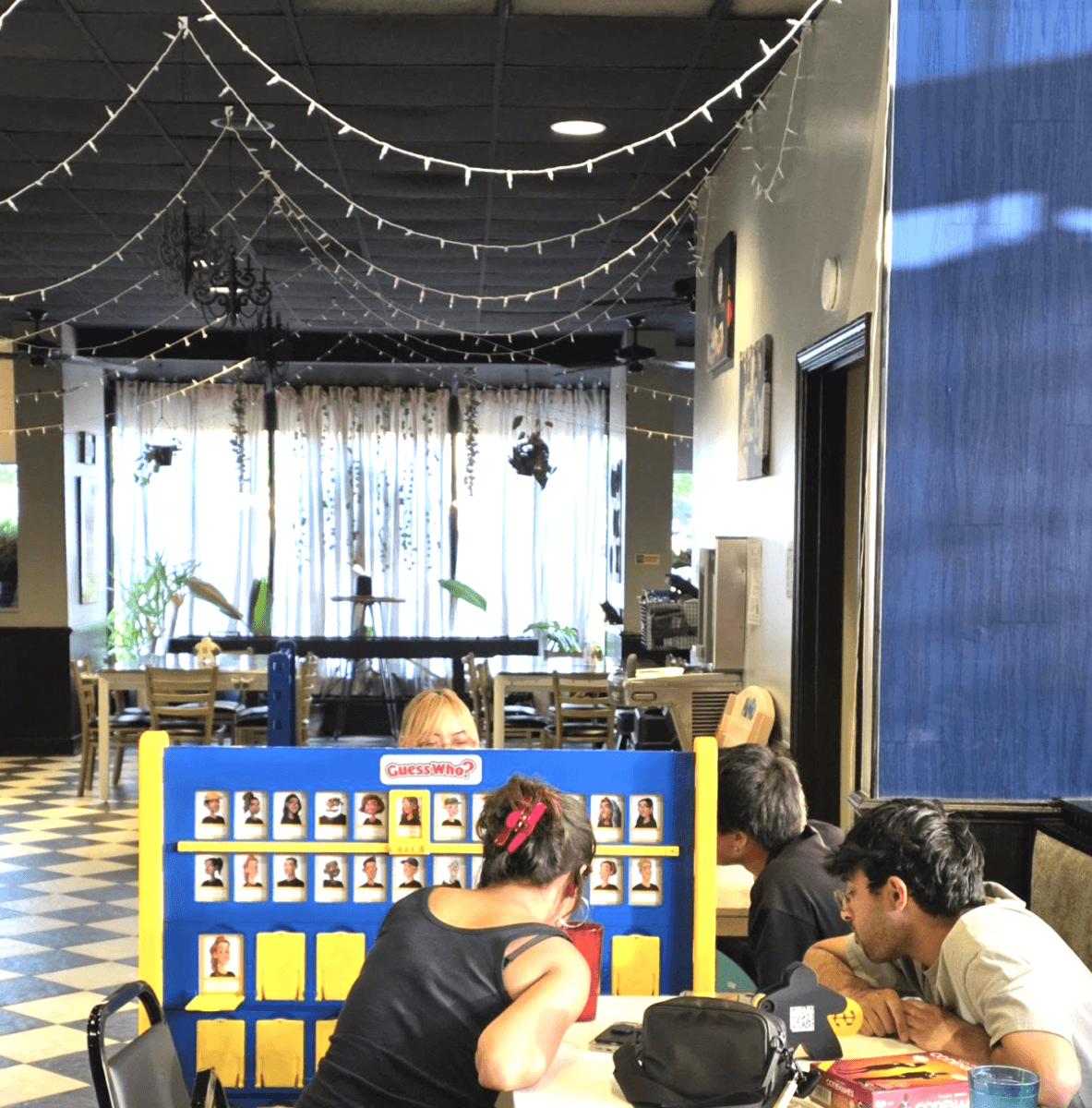 It's Playtime, Memphis! Here's Where to Get Your Game On - 4 Three people sit at a table playing the board game Guess Who? in a restaurant with checkered floors and string lights overhead.