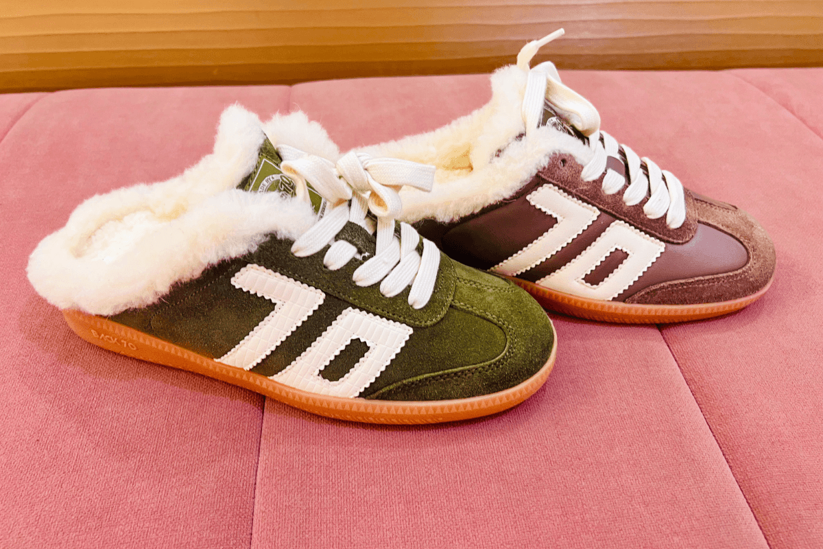 A pair of fleece-lined sneakers with white laces, green and brown suede panels, and white “70” detailing on the sides, placed on a pink cushioned surface.