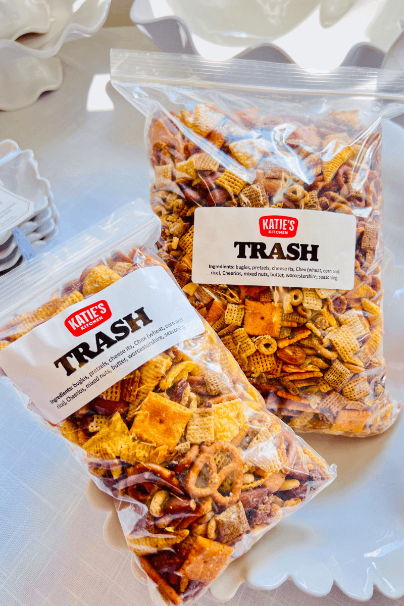 Two clear bags labeled “Katie’s Trash” contain a snack mix of crackers, pretzels, cereal, and nuts, displayed on a white surface.