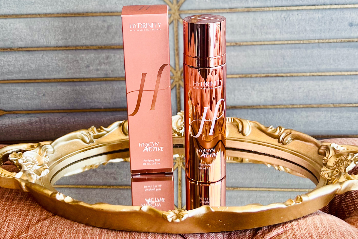 Hydrinity Hydration Active Purifying Mist bottle with its box displayed on an ornate gold tray in front of a wooden background.