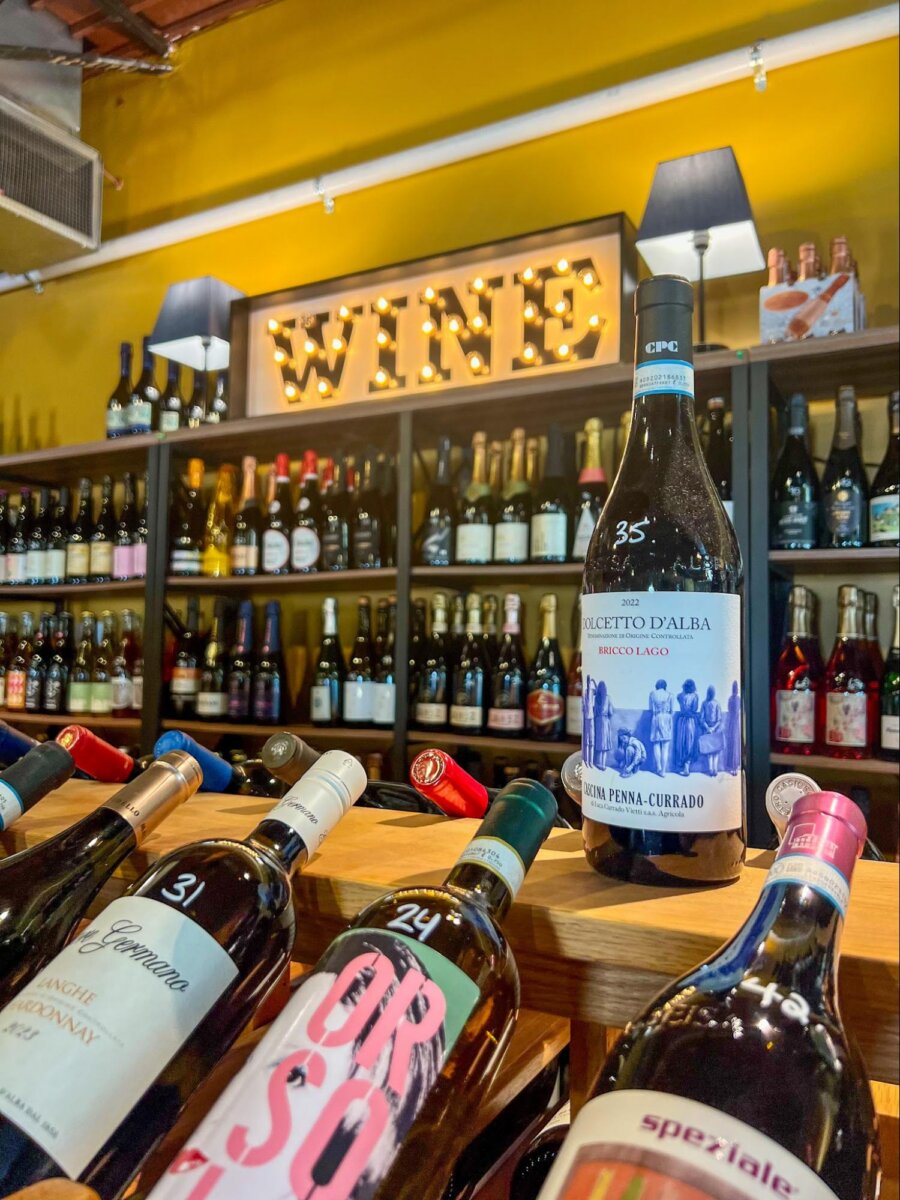 A selection of wine bottles on display in a store, with shelves of wine in the background and a lit “WINE” sign above.