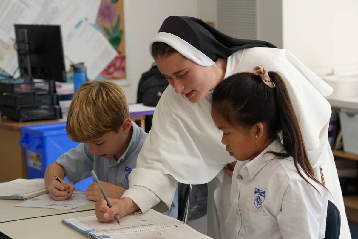Nashville Private School Open House Dates - 10 A nun helps two young students with their schoolwork at a classroom desk. Both children are writing in notebooks, and all three wear school uniformsβa common scene in private schools.