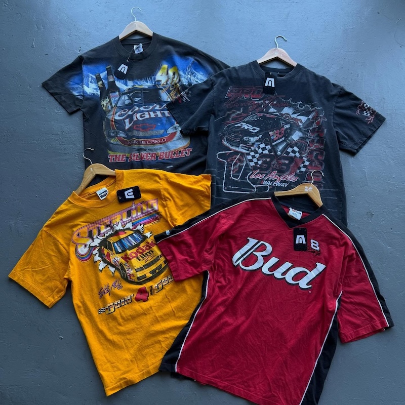 9 New Nashville Retail Spots to Explore - 8 Four racing-themed T-shirts, featuring bold graphics, are laid out flat on a gray surface, each on a hangerβa must-see for anyone exploring new retail spots or looking to add some flair to their Nashville shopping experience.