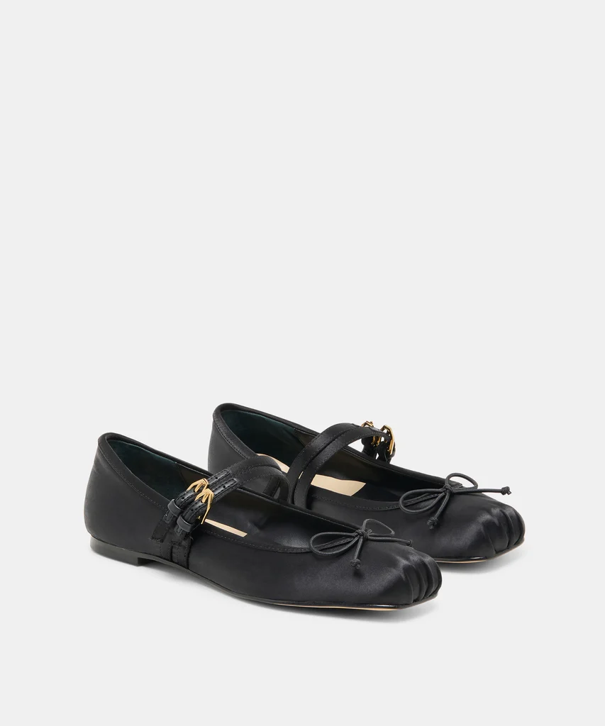 A pair of black leather ballet flats with a gathered toe, bow detail, ankle strap, and gold buckle—perfectly embodying fall trends—displayed on a plain background.