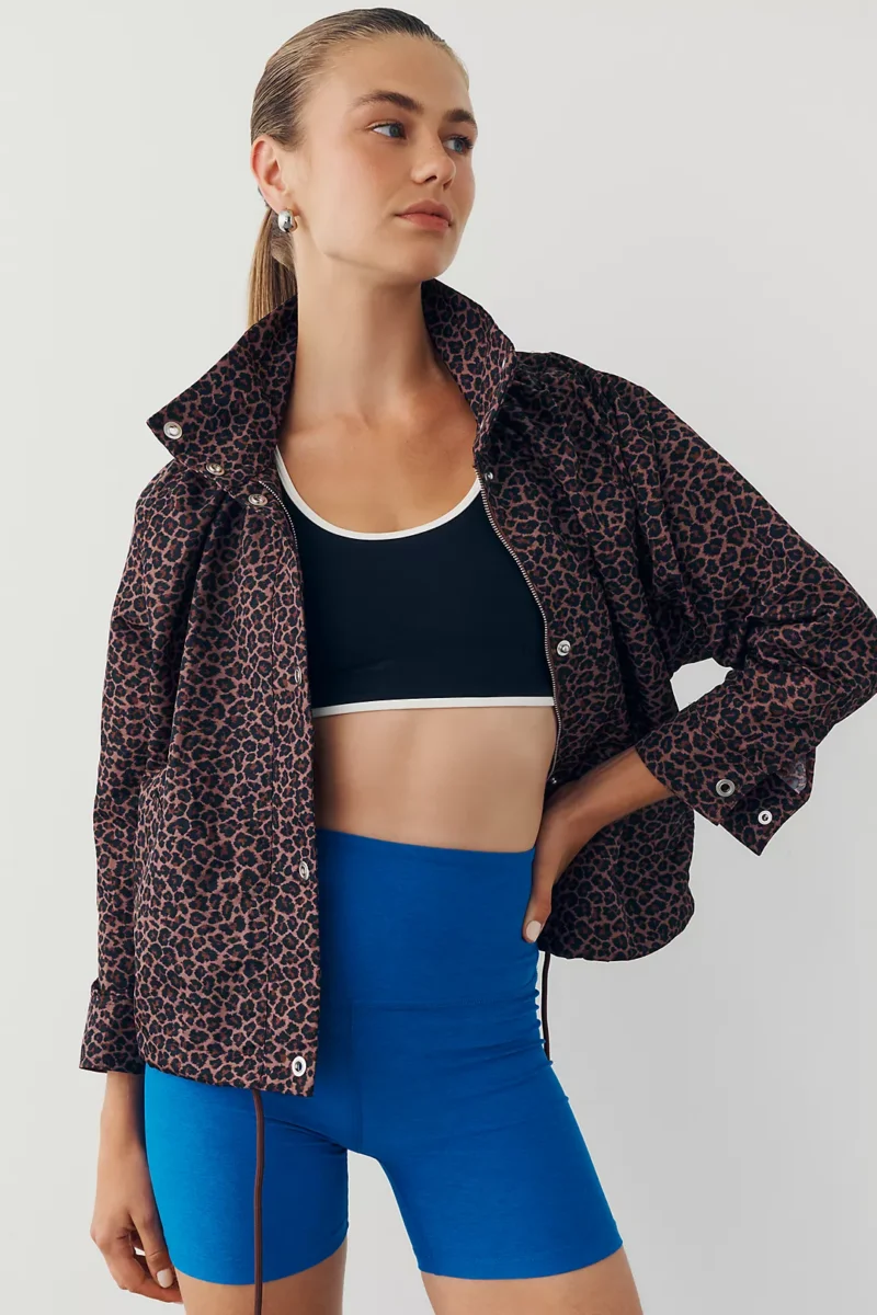 Woman stands against a plain background wearing a leopard print jacket, black sports bra with white trim, and blue high-waisted bike shorts—a bold Ready to Wear look that captures the essence of Fall Trends.