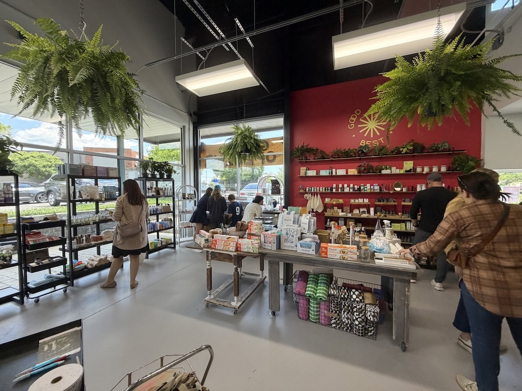 9 New Nashville Retail Spots to Explore - 4 People shop in a well-lit Nashville retail store with large windows, shelves of products, and hanging plants. A table displays various items in the center. Some customers browse while others check out, enjoying one of the cityβs inviting new retail spots for Nashville shopping.