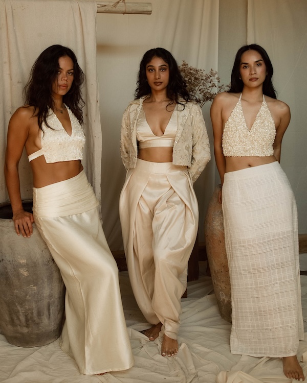 9 New Nashville Retail Spots to Explore - 2 Three women stand indoors wearing cream-colored, elegant outfits with skirts and pants, posing against a neutral background with pottery and draped fabricβa scene reminiscent of the fresh style found in new retail spots on the Nashville shopping scene.
