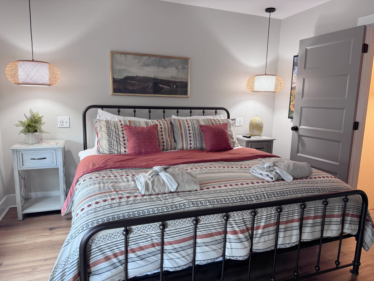 Bedroom with a neatly made bed, patterned bedding, two bathrobes, nightstands, hanging lamps, a plant, and framed artwork on the wall—creating the perfect retreat for North Alabama glamping.