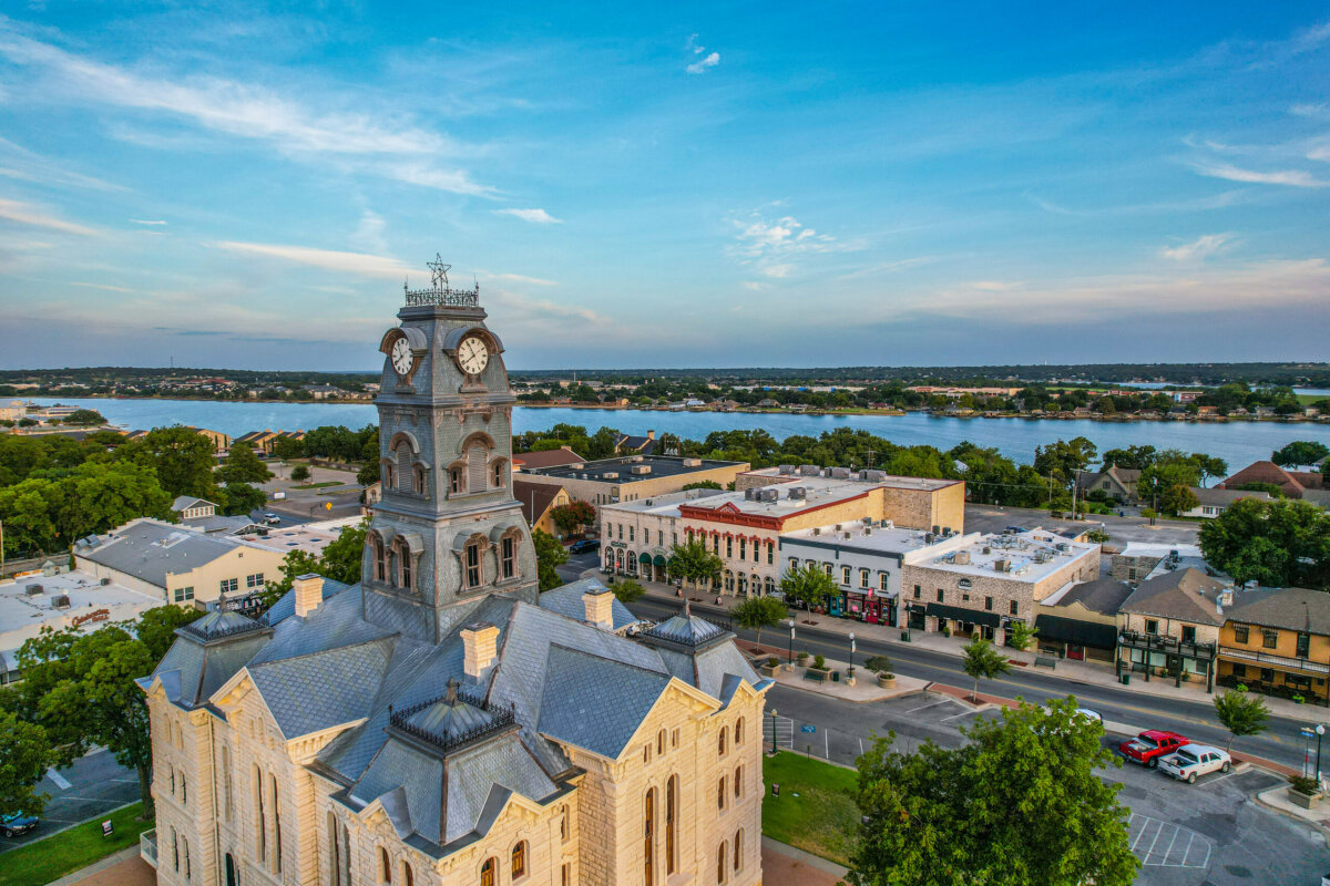 5 Destinations Where Southern Charm Thrives - 10 Aerial view of a historic courthouse with a clock tower in a small town, set near a large body of water under a blue sky.