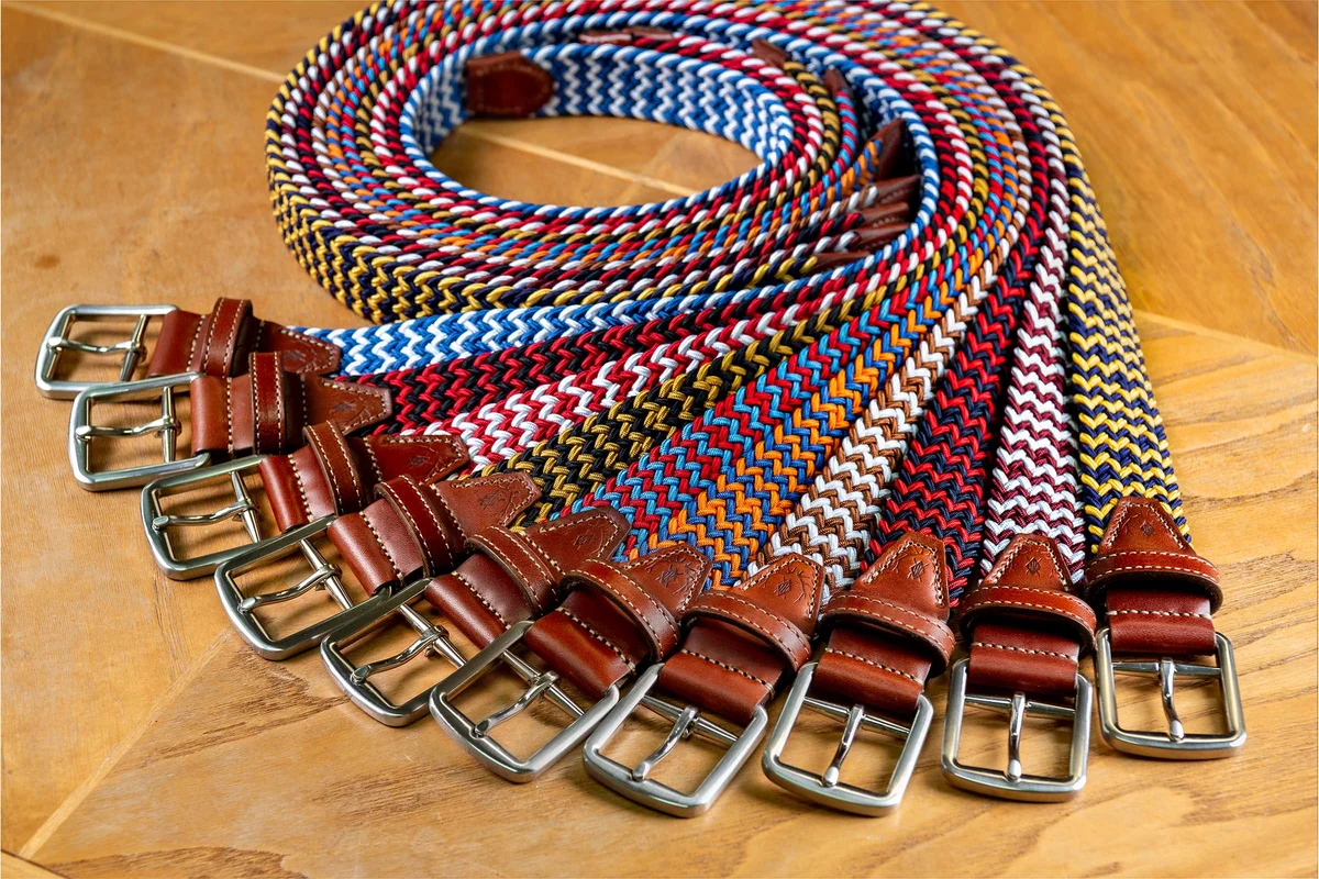 Southern Brands to Know for Football Season: Clothing, Decor & More - 12 Several colorful woven belts with brown leather tips and metal buckles are arranged side by side on a wooden surface, making these accessories perfect for adding a vibrant touch to your football season wardrobe.