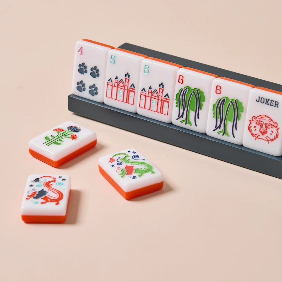 Southern Brands to Know for Football Season: Clothing, Decor & More - 7 Six mahjong tiles stand in a rack, displaying various symbols and numbers; three more tiles with illustrations are laid out in front on a light surface, creating an entertaining arrangement that could be the perfect accessory for gatherings during football season.