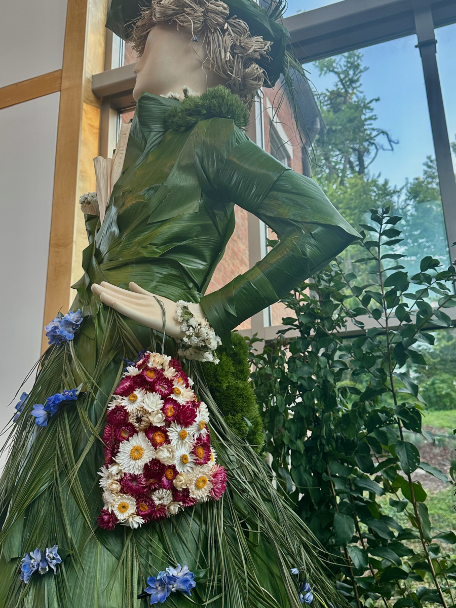 Fleurs de Villes: Cheekwood’s Latest Exhibit is a Must-See - 5 A mannequin dressed in an outfit made from green leaves and decorated with colorful flowers stands indoors near large windows, evoking the natural beauty often seen at Cheekwood.