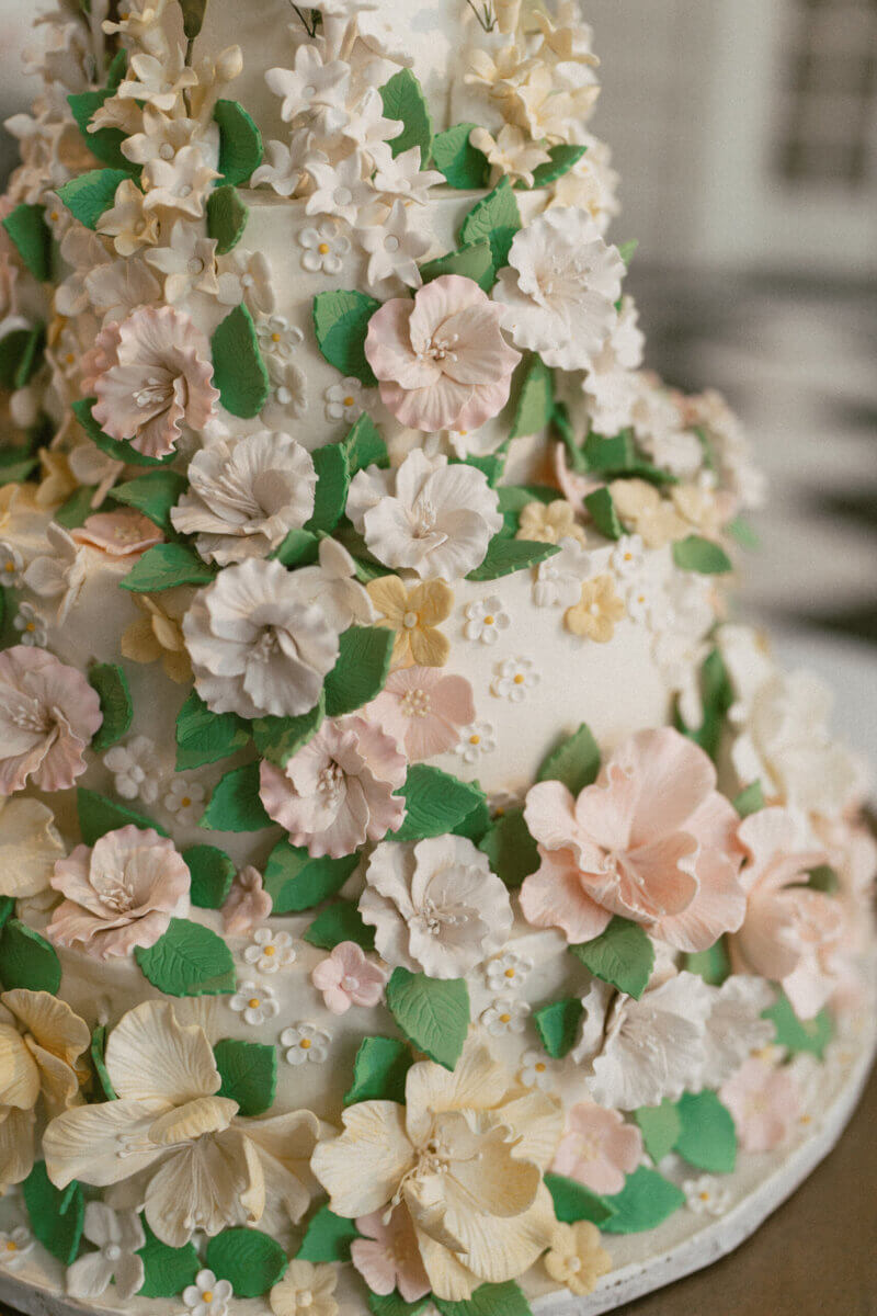 A Country Club Wedding with Show-Stopping Bridal Fashion & Peonies for Days - 11 Three-tiered cake decorated with intricate pastel-colored sugar flowers and green leaves, perfect for a classic wedding or an elegant celebration at the Belle Meade Country Club during your Nashville wedding.