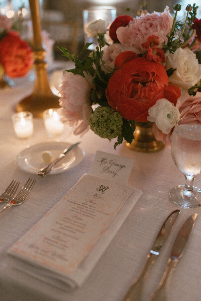 A Country Club Wedding with Show-Stopping Bridal Fashion & Peonies for Days - 20 Elegant table setting with a floral centerpiece, menu, place card, glass of water, candles, bread plate with butter, and silverware on a white tablecloth—perfect for a classic wedding at Belle Meade Country Club in Nashville.
