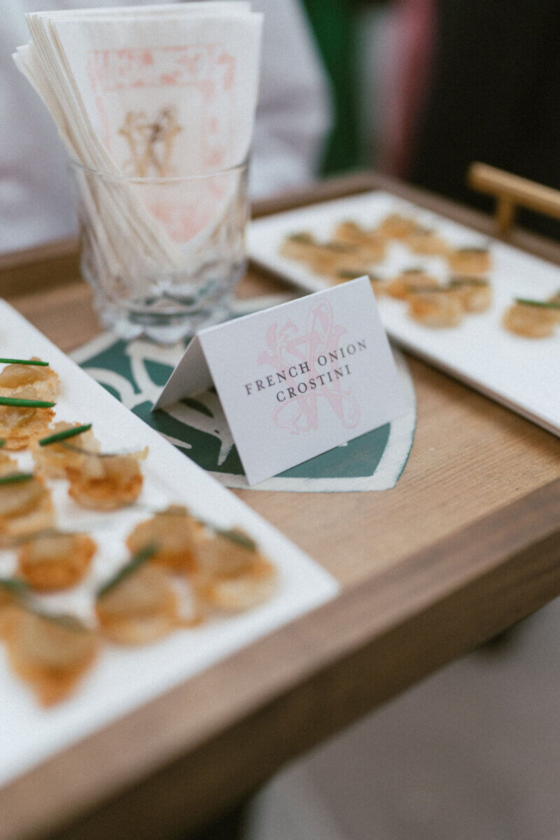A Country Club Wedding with Show-Stopping Bridal Fashion & Peonies for Days - 18 A tray with plates of French onion crostini, a glass holding napkins, and a card labeled “French Onion Crostini,” perfectly captures the elegant charm of a classic wedding at Belle Meade Country Club in Nashville.