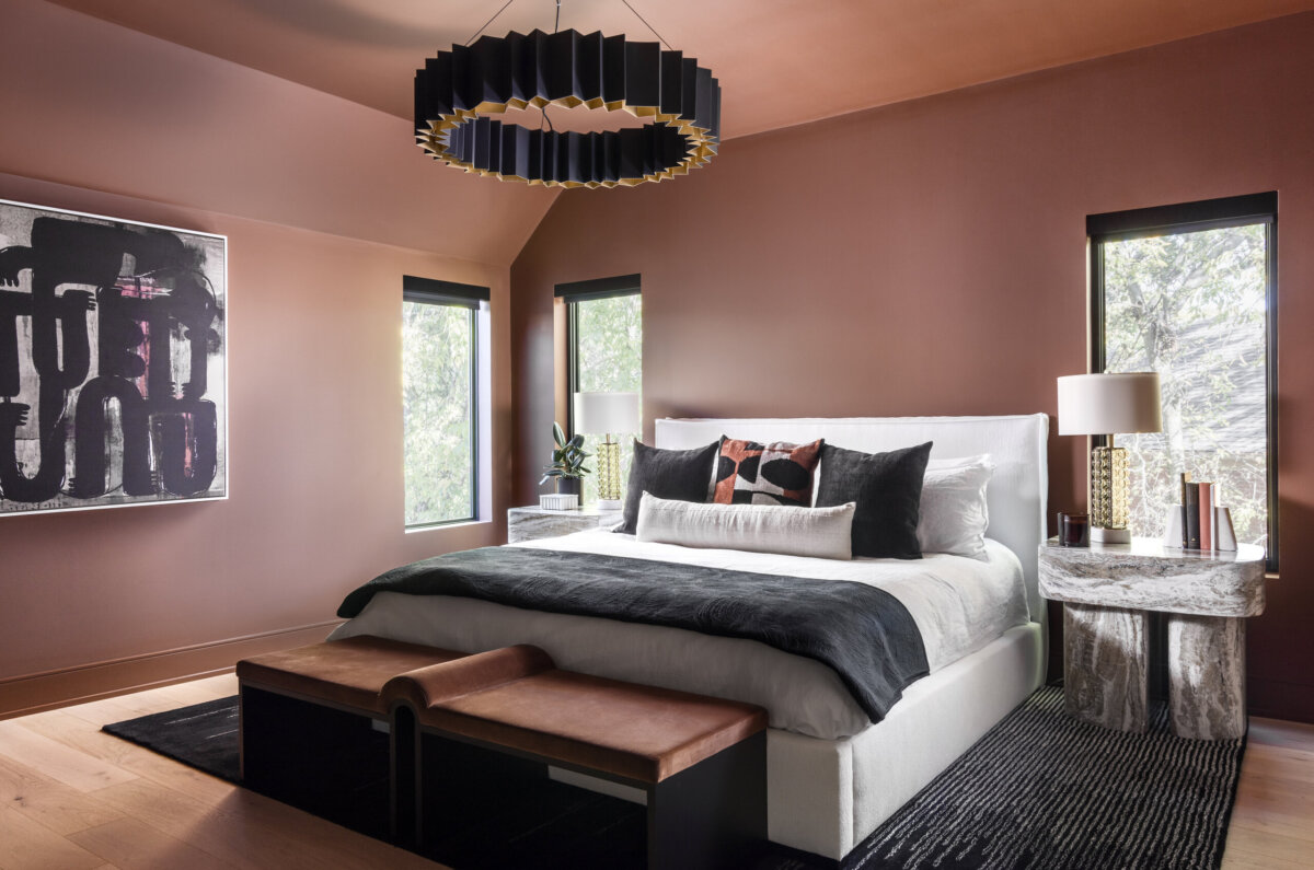 There's a Graffiti-Covered Bust in This Nashville Home, and It Works - 15 A modern bedroom reminiscent of a modern art gallery, featuring brown walls, a white bed, abstract art, two marble side tables with lamps, and a black and gold chandelier—perfect for a striking home in Nashville.