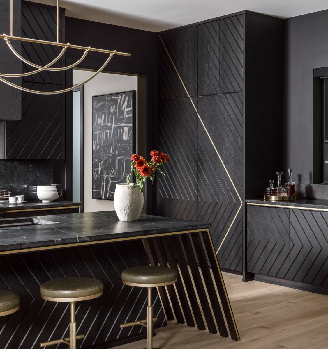 There's a Graffiti-Covered Bust in This Nashville Home, and It Works - 8 Modern kitchen with black cabinets, gold accents, an island with matching stools, and a white vase with red flowers centered on the counter. Abstract black-and-white art hangs in the background, giving this Nashville home the ambiance of a modern art gallery.
