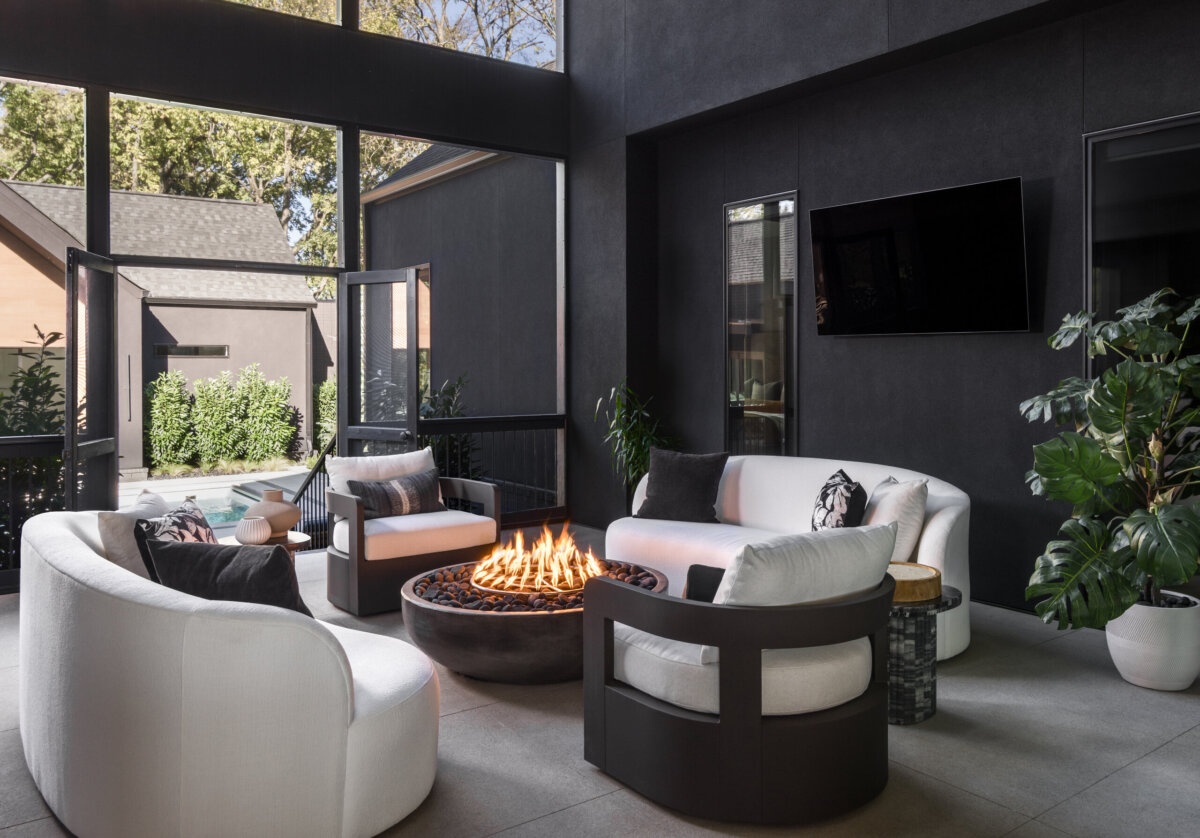 There's a Graffiti-Covered Bust in This Nashville Home, and It Works - 18 This striking home features a modern outdoor patio with two white sofas and two black armchairs arranged around a circular fire pit, large potted plants, a wall-mounted TV, and open doors leading to a lush garden area—evoking the sophisticated ambiance of a modern art gallery.